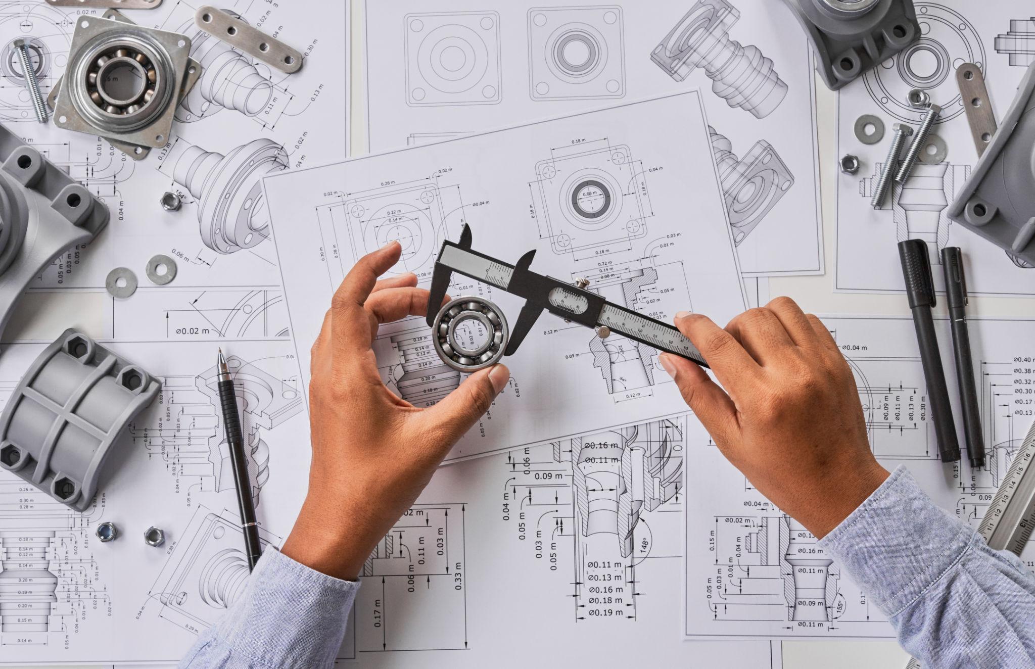 Engineer measuring a component with calipers over technical engineering drawings