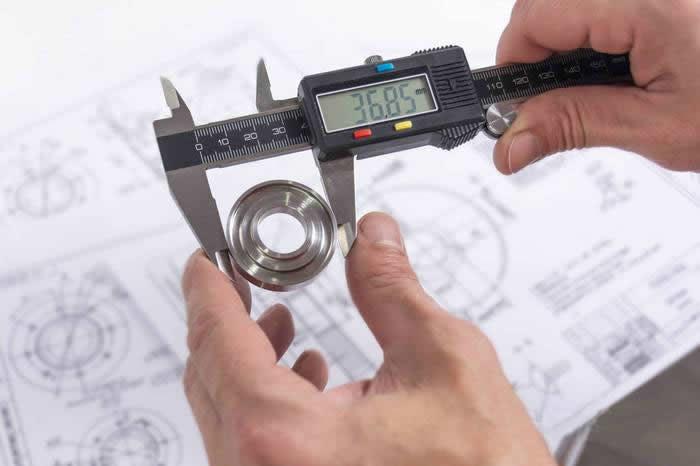 Digital calipers measuring a precision machined component over engineering drawings